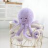 Une peluche de poulpe violette avec des tentacules blancs sur un tabouret en métal doré.