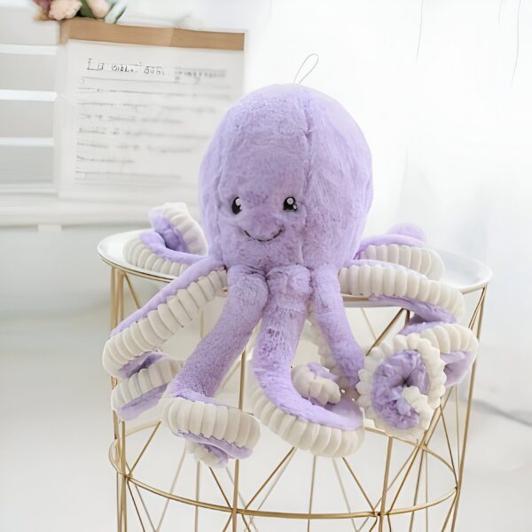 Une peluche de poulpe violette avec des tentacules blancs sur un tabouret en métal doré.