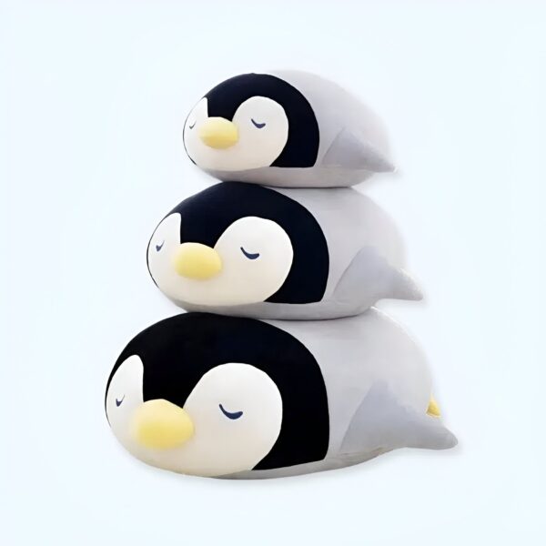 Trois adorables peluches pingouins empilées les unes sur les autres. Les pingouins ont les yeux fermés et ont l'air de dormir.