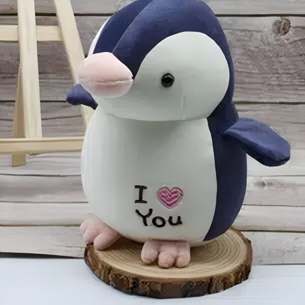 Un adorable manchot en peluche blanc et bleu avec un cœur rose sur le ventre et l'inscription "Je t'aime".