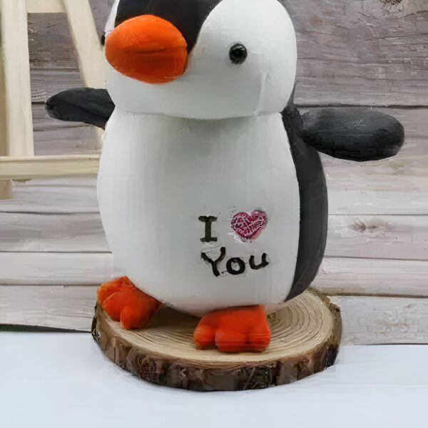 Un pingouin en céramique blanc avec un cœur rose et l'inscription "Je t'aime" sur un rondin de bois.