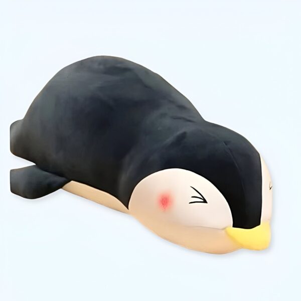 Un manchot en peluche noir et blanc allongé sur le ventre, les yeux fermés.