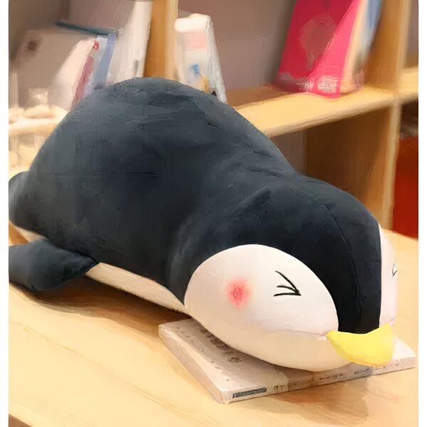 Un gros pingouin en peluche noir et blanc allongé sur un livre sur une table en bois.