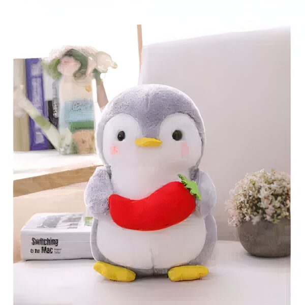 Un manchot en peluche gris tenant une carotte rouge.