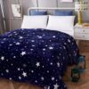 peluche-plaid-etoiles-lumineuses-bleu-nuit-2a-2 Une couverture bleue foncée avec des étoiles blanches. La couverture est sur un lit avec des oreillers blancs.