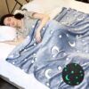 Une femme dort sous une couverture bleue avec des étoiles et des lunes blanches. Les étoiles et la lune brillent dans le noir.
