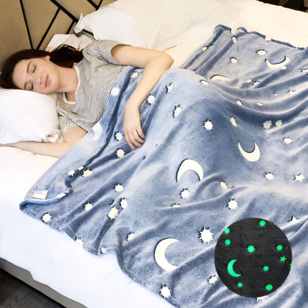 Une femme dort sous une couverture bleue avec des étoiles et des lunes blanches. Les étoiles et la lune brillent dans le noir.
