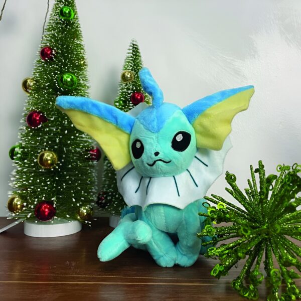 peluche-pokemon-evoli-et-aquali-pack-de-2-3a-1 Une peluche de Vaporeon, un Pokémon de type Eau, assis près de deux arbres de Noël décorés de boules rouges et dorées.