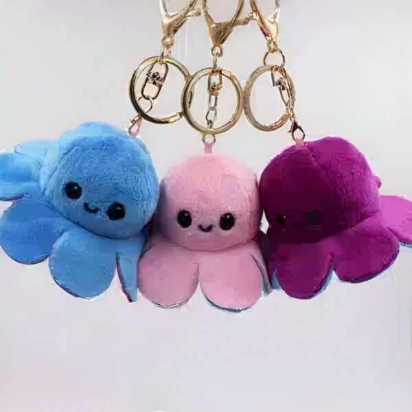 Trois adorables peluches de poulpe, une bleue, une rose et une violette, sont attachées à un porte-clés doré.