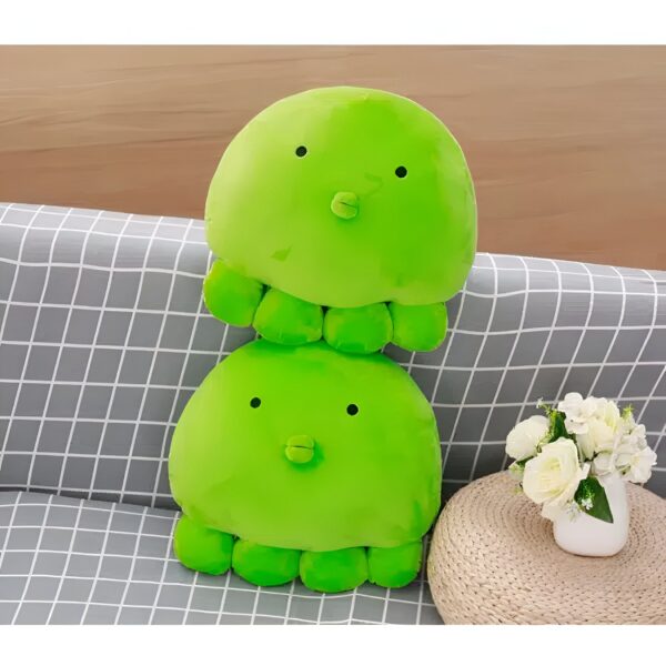 Deux adorables peluches poulpes verts empilées sur un canapé gris à carreaux.