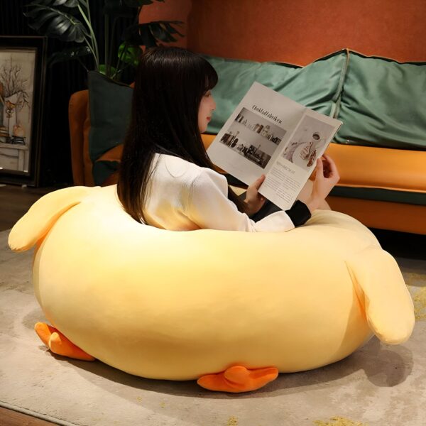 Une femme assise dans un fauteuil en forme de canard jaune en peluche, lisant un livre.