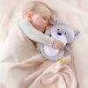 Un bébé endormi dans une couverture douce, serrant un adorable ours en peluche avec un projecteur de lumières étoilées.