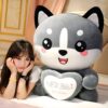 peluche-renard-geant-2a-2 Une jeune femme souriante avec un grand ourson en peluche gris en forme de chien tenant un cœur brodé avec "Joyeux anniversaire" en chinois et en anglais.