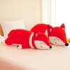 Deux peluches en forme de renard rouge allongées sur un lit blanc.