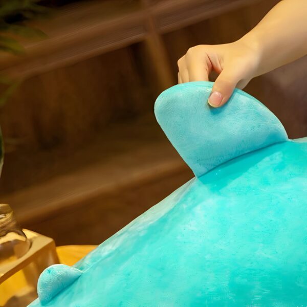 Une main touche une grande peluche turquoise en forme de dauphin.