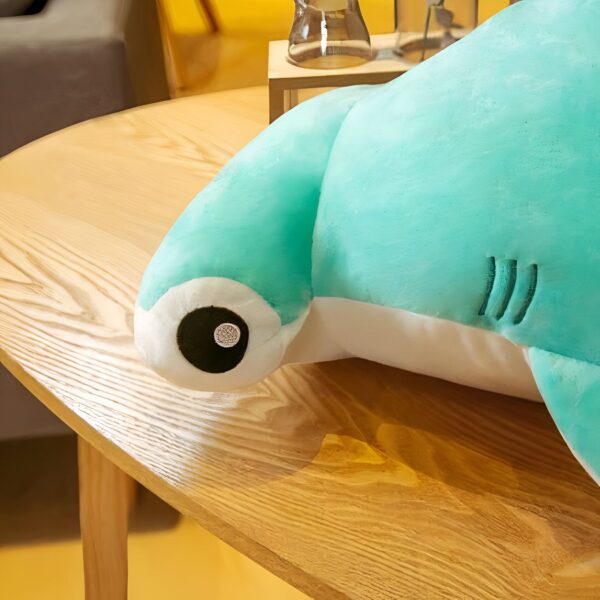 Un coussin en forme de requin marteau turquoise sur une table en bois.