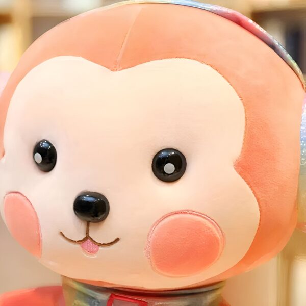 Gros plan sur le visage d'un singe en peluche rose avec de grands yeux noirs et un petit nez noir.