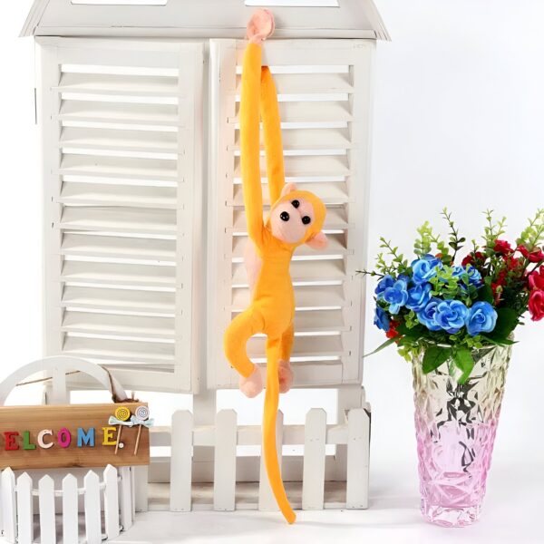 Un singe en peluche jaune suspendu à une porte blanche avec un vase de fleurs bleues et roses en arrière-plan.