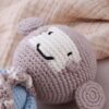 peluche-singe-tricot-jouet-en-peluche-tricote-de-haute-qualite-cadeau-pour-enfants-2a-2 Un singe en tricot rose avec un sourire brodé, reposant sur une couverture en coton doux.