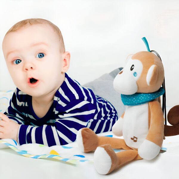 Un bébé en chemise rayée bleue et blanche se trouve à côté d'un singe en peluche avec un foulard bleu. Le singe a une note de musique sur son ventre.