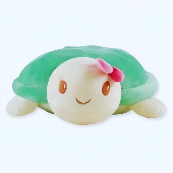 Une tortue en peluche verte avec un visage souriant et un nœud rose.