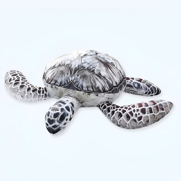 Une peluche de tortue marine avec une carapace grise et des motifs noirs. Elle a de grands yeux noirs et des pattes grises et blanches.