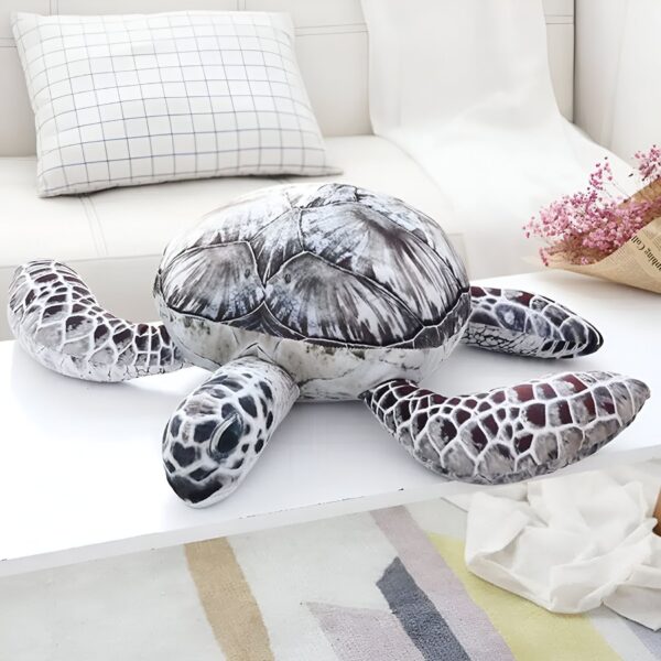 Une grande peluche en forme de tortue marine posée sur une table. La tortue est grise et blanche, avec une carapace détaillée.