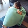 Une jeune femme s'assoit dans un fauteuil vert et moelleux, le visage caché par le coussin. Elle semble relaxée et confortable.