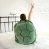 Une jeune femme assise sur un lit avec un coussin en forme de carapace de tortue. Elle a les bras levés et fait un signe de la paix.