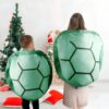Deux enfants portent des costumes de tortue, l'un vert et l'autre bleu, devant un arbre de Noël.