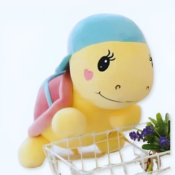 Une adorable peluche de tortue jaune avec une coquille rose et un bandana bleu. Elle a de grands yeux noirs et un sourire amical.
