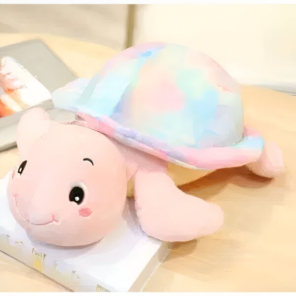 Une tortue en peluche rose avec une coquille arc-en-ciel posée sur un livre.