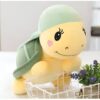 Une adorable peluche de tortue jaune avec une carapace verte, des yeux noirs et un petit cœur rose sur la joue, assis dans un panier blanc.