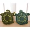 Deux tortues en peluche vertes avec des coquilles jaunes. Les tortues sont posées sur un plancher en bois.
