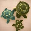 Trois tortues en peluche de différentes tailles sur un fond en bois.