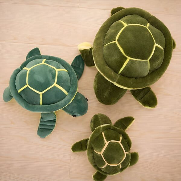 Trois tortues en peluche de différentes tailles sur un fond en bois.