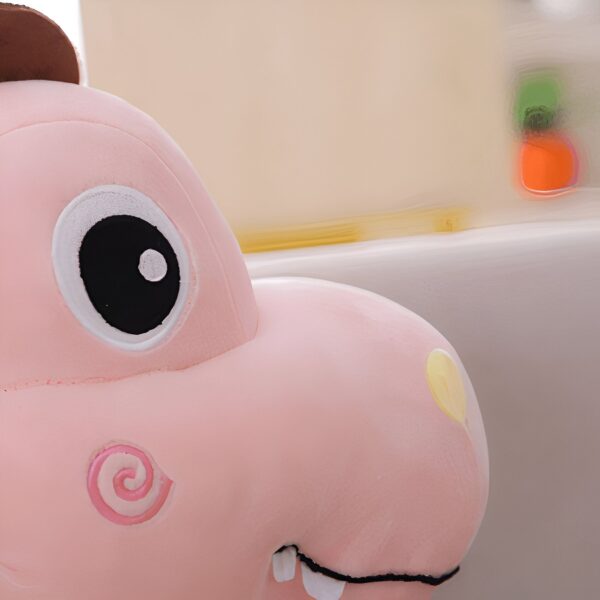 Gros plan sur la tête d'une peluche rose en forme de dinosaure avec un œil noir et blanc et une bouche ouverte montrant des dents.