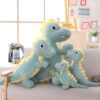 Quatre dinosaures en peluche de différentes tailles, assis sur un canapé gris. Les dinosaures sont verts avec des détails jaunes et ont des expressions mignonnes.