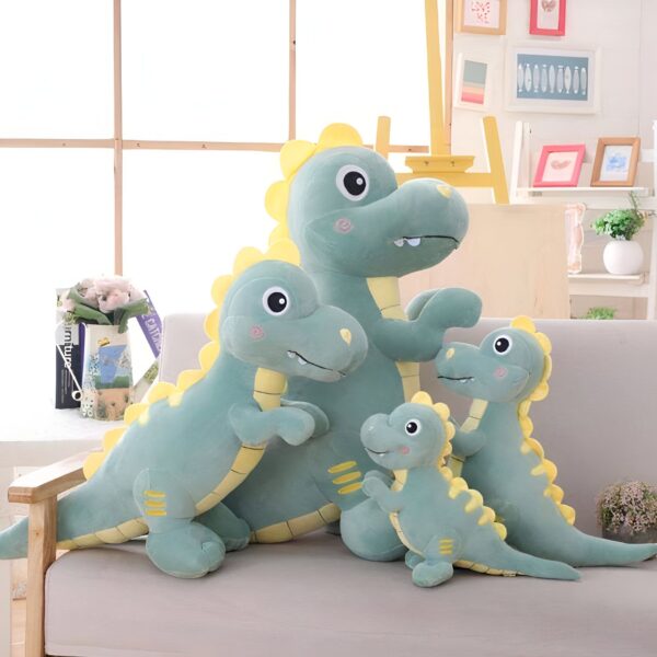 peluche-tyrannosaurus-rex-vert-doudou-dino-pour-bebe-1a-2 Quatre dinosaures en peluche de différentes tailles, assis sur un canapé gris. Les dinosaures sont verts avec des détails jaunes et ont des expressions mignonnes.