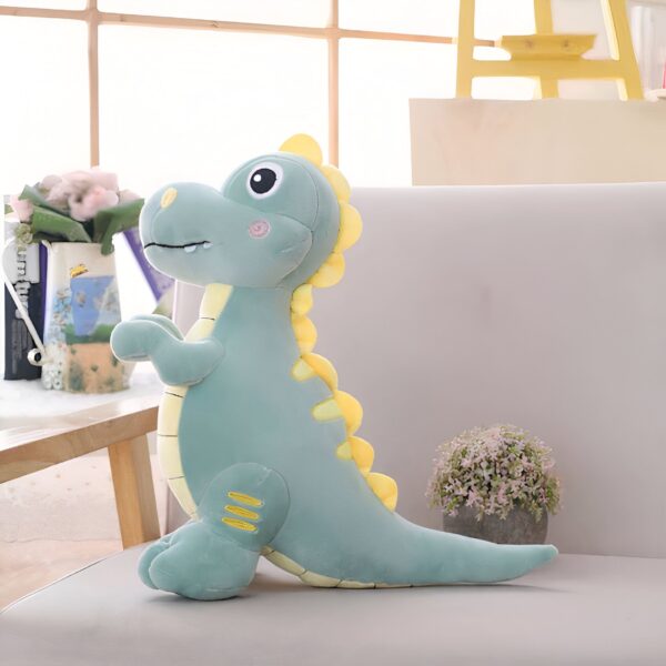 Une peluche de dinosaure vert avec des détails jaunes assis sur un canapé blanc.