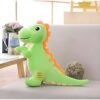 Une peluche verte en forme de dinosaure avec des détails orange sur un fauteuil gris.