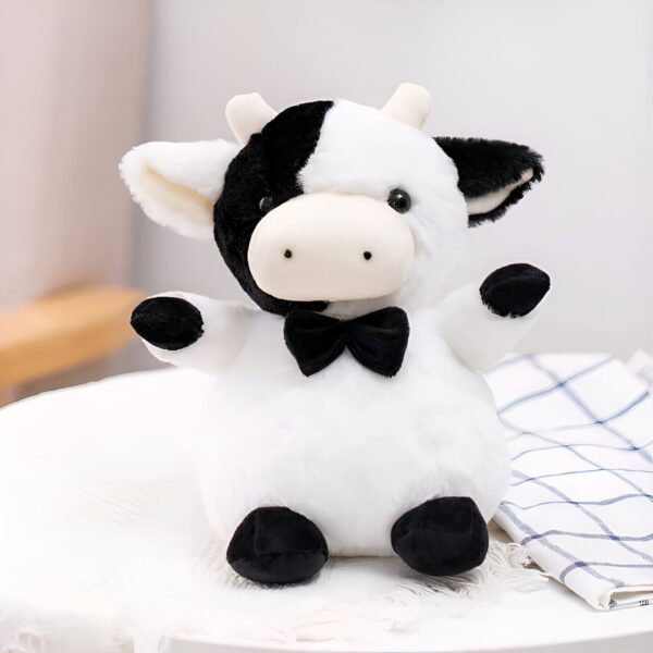Une peluche vache blanche et noire avec un nœud papillon noir.