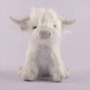 Une peluche blanche en forme de vache écossaise assise sur un fond violet.