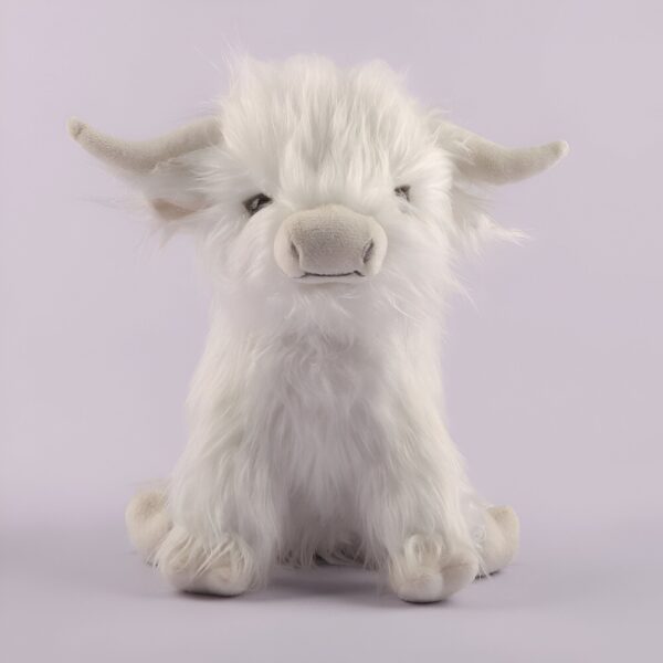 Une peluche blanche en forme de vache écossaise assise sur un fond violet.