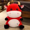 Une peluche de vache rouge avec de grands yeux noirs, un sourire brodé et trois cœurs multicolores brodés sur son ventre.
