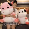 Une jeune femme tenant deux peluches en forme de vache, une rose et une blanche, avec des petits cœurs brodés.