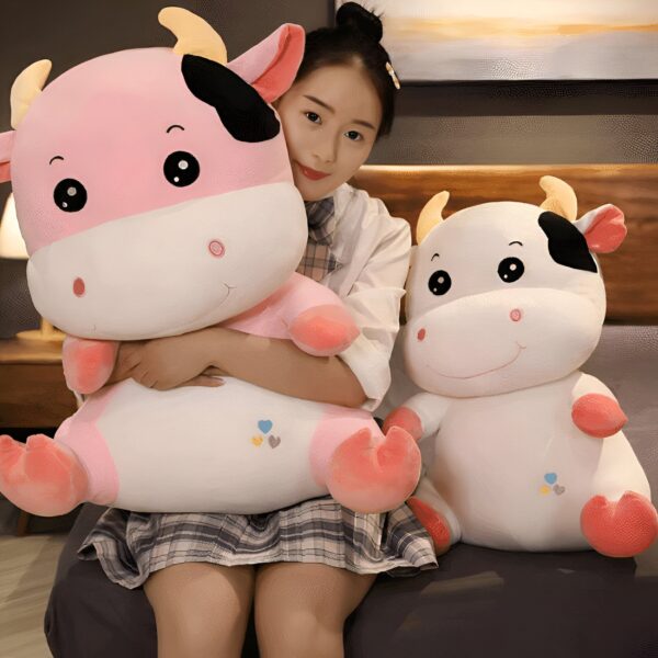 Une jeune femme tenant deux peluches en forme de vache, une rose et une blanche, avec des petits cœurs brodés.