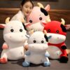 Une femme souriante tenant quatre peluches de vache en forme de jouet. Les peluches sont blanches, rouges, bleues et roses.
