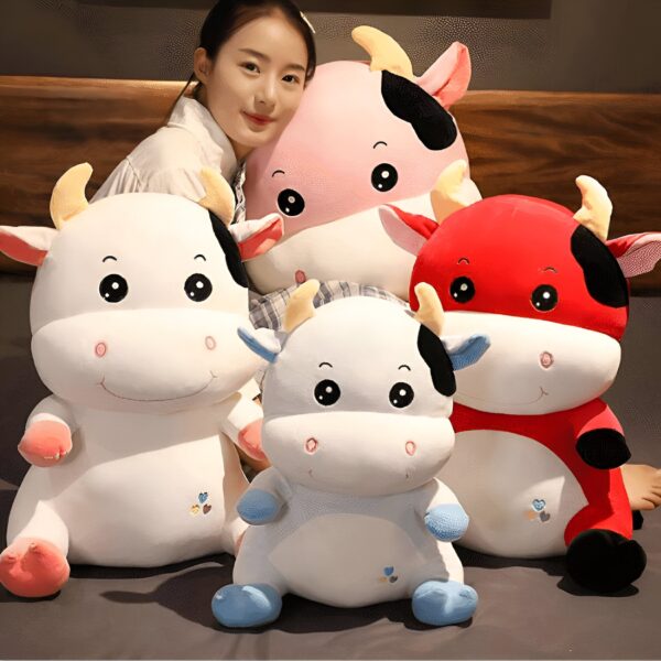 Une femme souriante tenant quatre peluches de vache en forme de jouet. Les peluches sont blanches, rouges, bleues et roses.