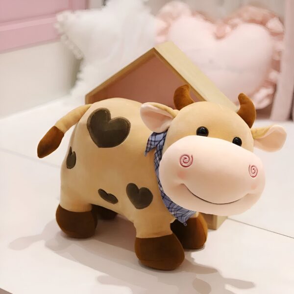 Une peluche de vache brune avec des cœurs noirs et un bandana bleu et blanc.
